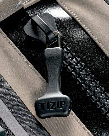 Close-up of a black TIZIP zipper pull on a beige and black fabric bag, showing the brand name embossed on the pull.