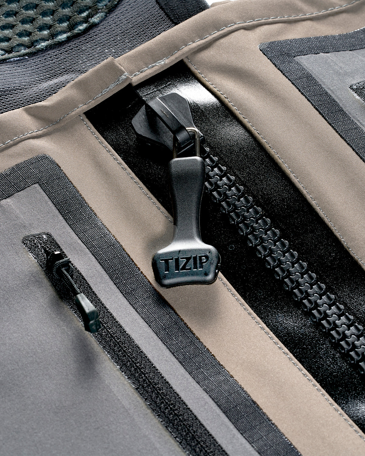 Simms G3Z Pro Stockingfoot Wader - Close-up of main prominent black TIZIP zipper, showing layered panels in taupe, gray, and black. With zippered chest pocket 