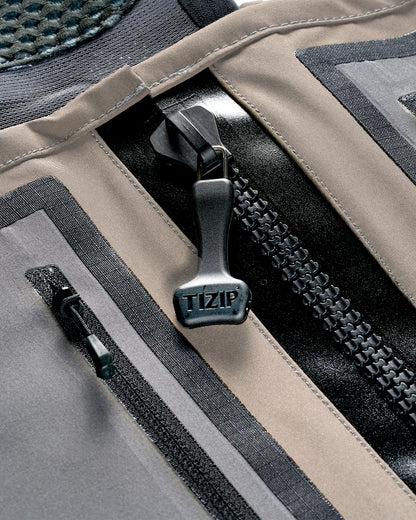 Simms G3Z Pro Stockingfoot Wader - Close-up of main prominent black TIZIP zipper, showing layered panels in taupe, gray, and black. With zippered chest pocket 