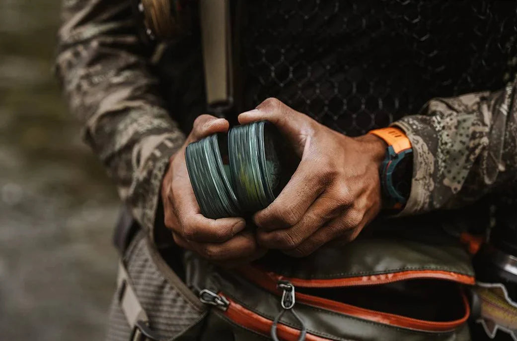 Angler holding a Fishpond Predator Fly Puck with Steelhead flies, wearing camouflage clothing and fishing gear